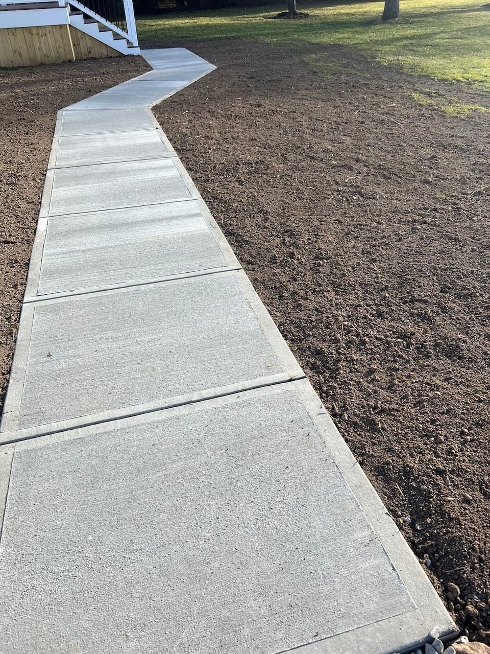 Curved concrete sidewalk extending from house stairs next to prepared soil