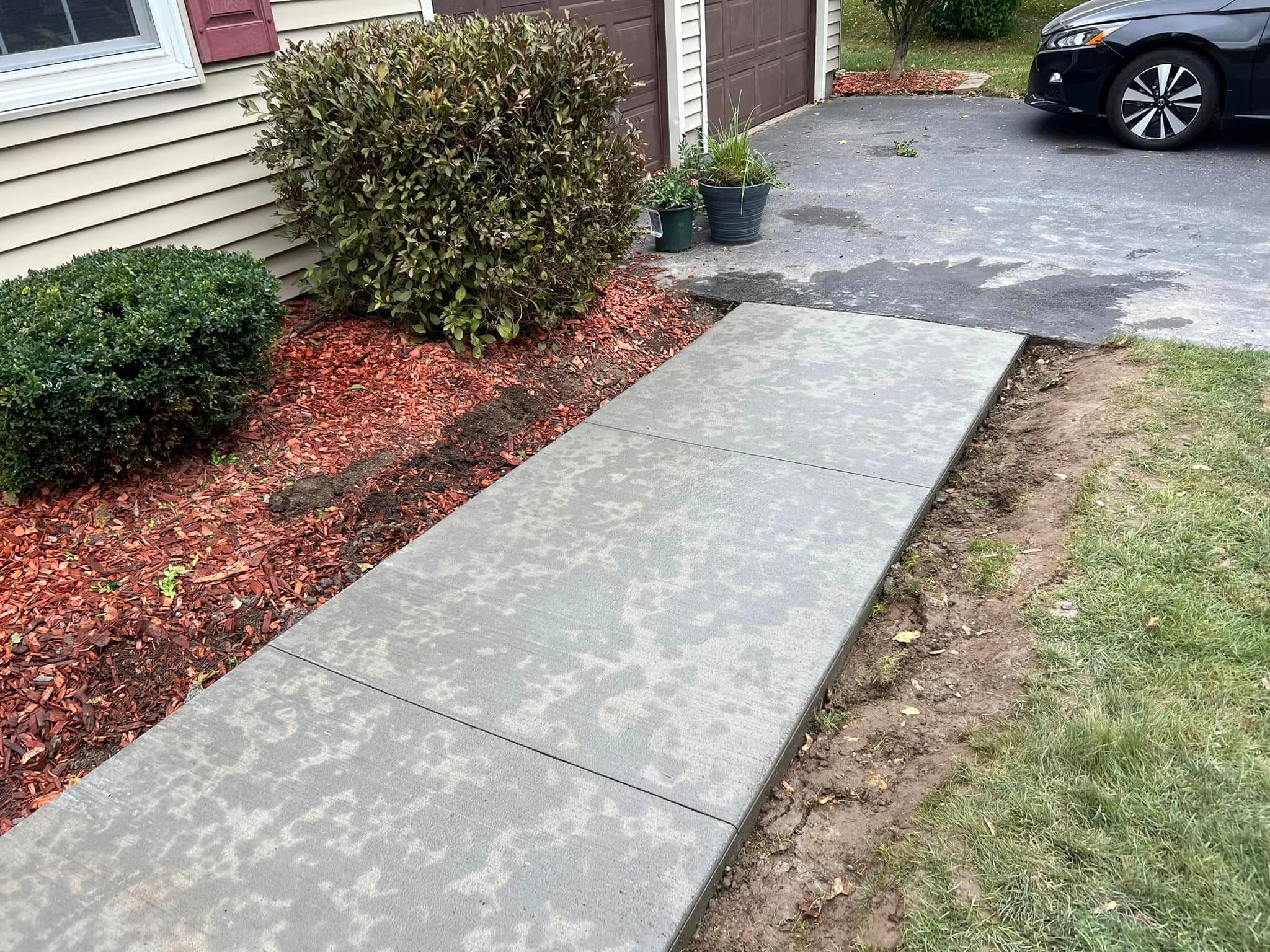 New concrete walkway beside landscaped garden bed with red mulch