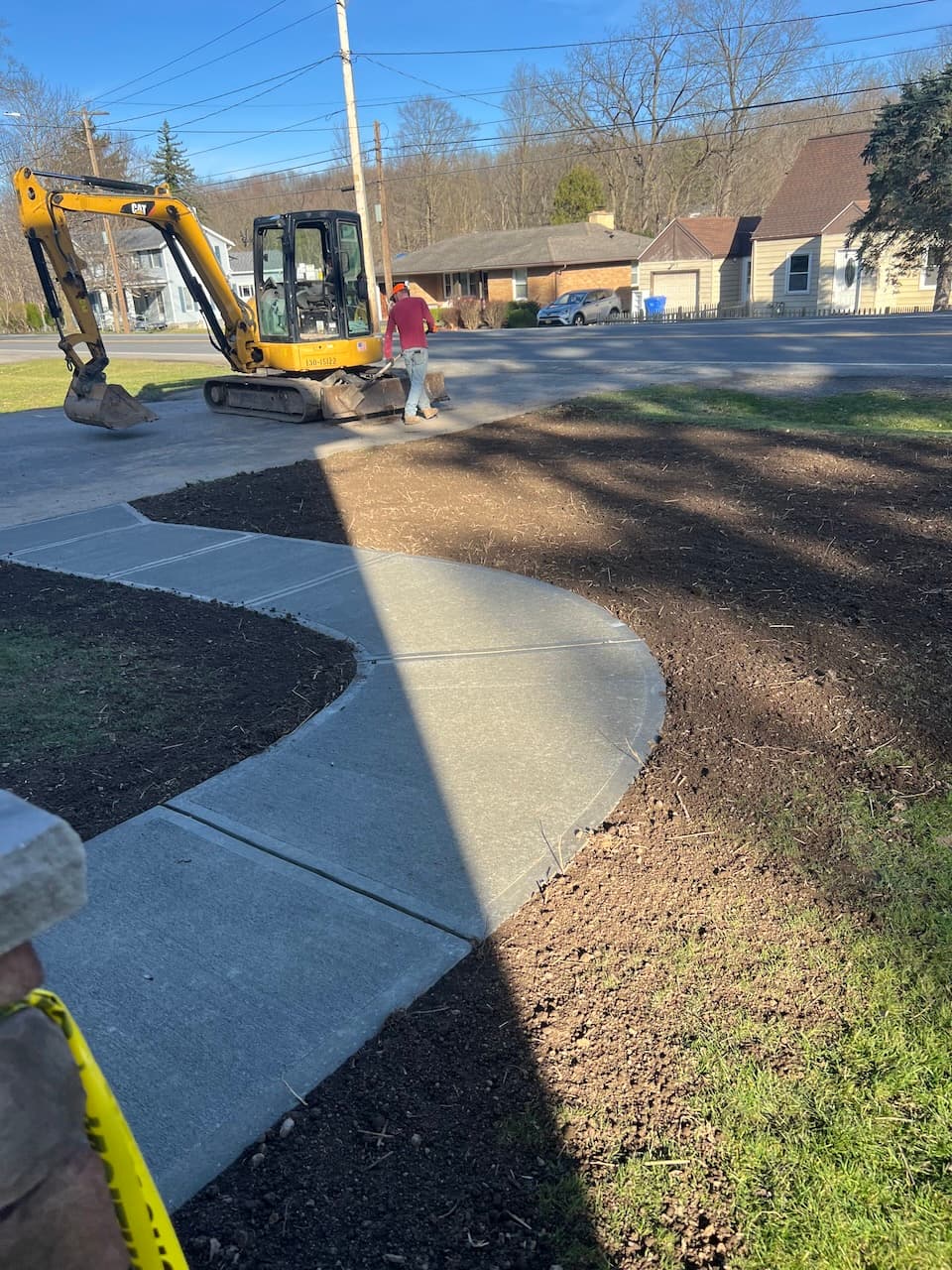 Curved concrete sidewalk with excavator and worker in residential area