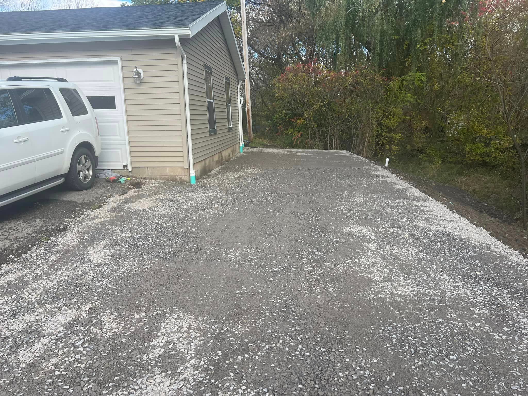 Newly poured concrete pad next to garage with white SUV parked nearby