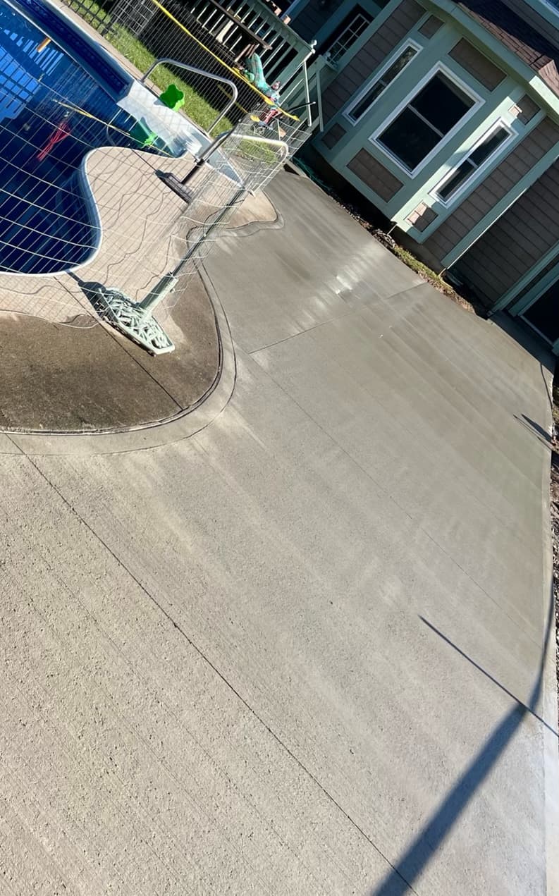 Freshly poured and finished concrete driveway leading to a gray house