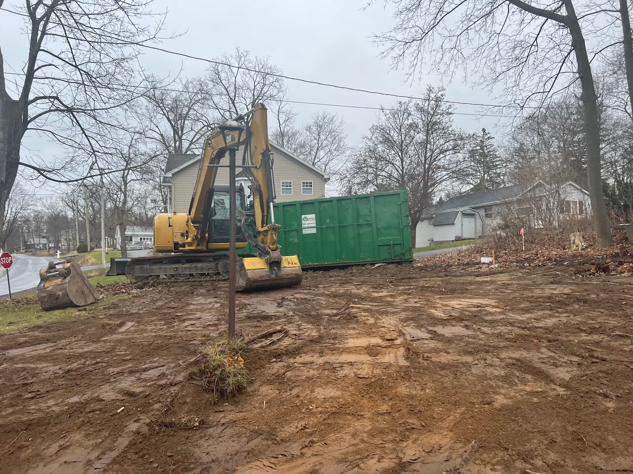 Yellow excavator and green dumpster on cleared residential construction site