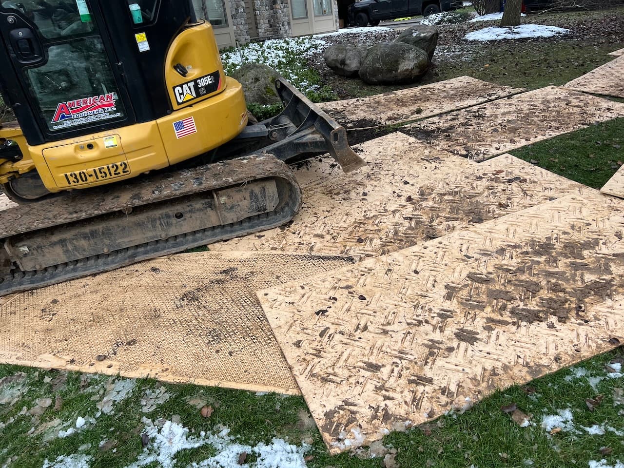 Yellow CAT excavator on OSB and mesh ground protection mats during site prep