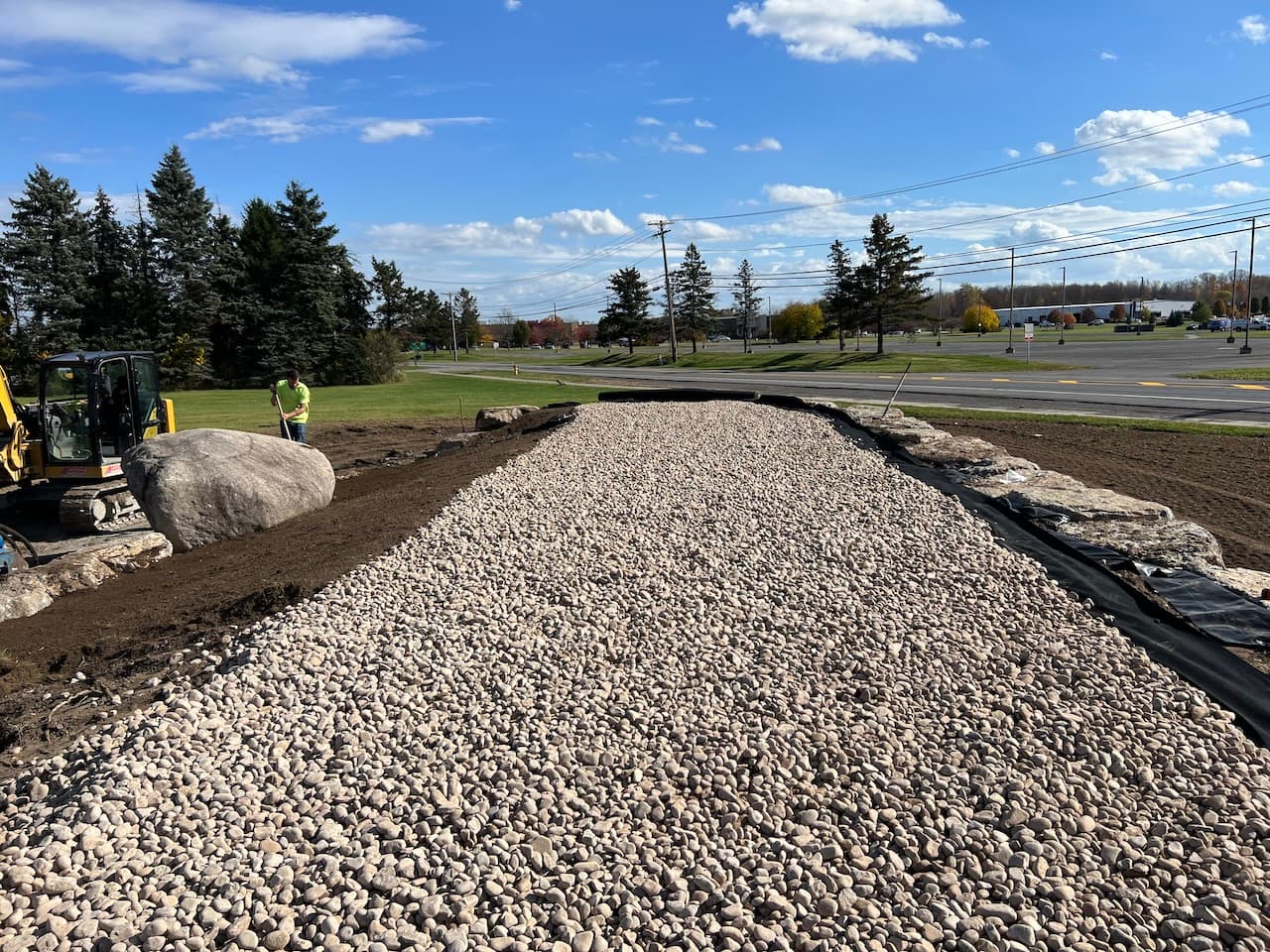 Gravel pathway installation with large boulders and excavation equipment