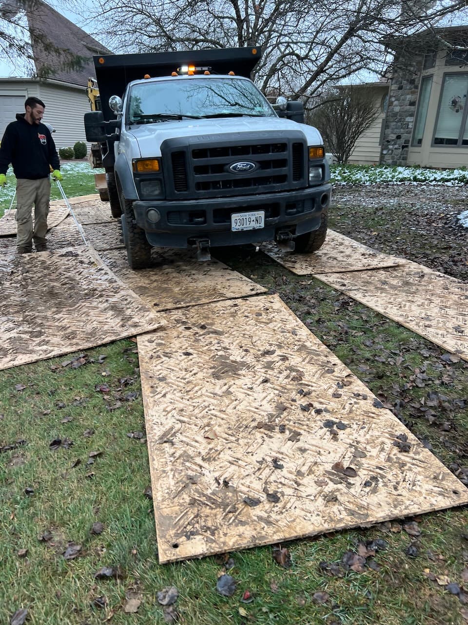 White Ford dump truck on plywood sheets laid across lawn to protect ground