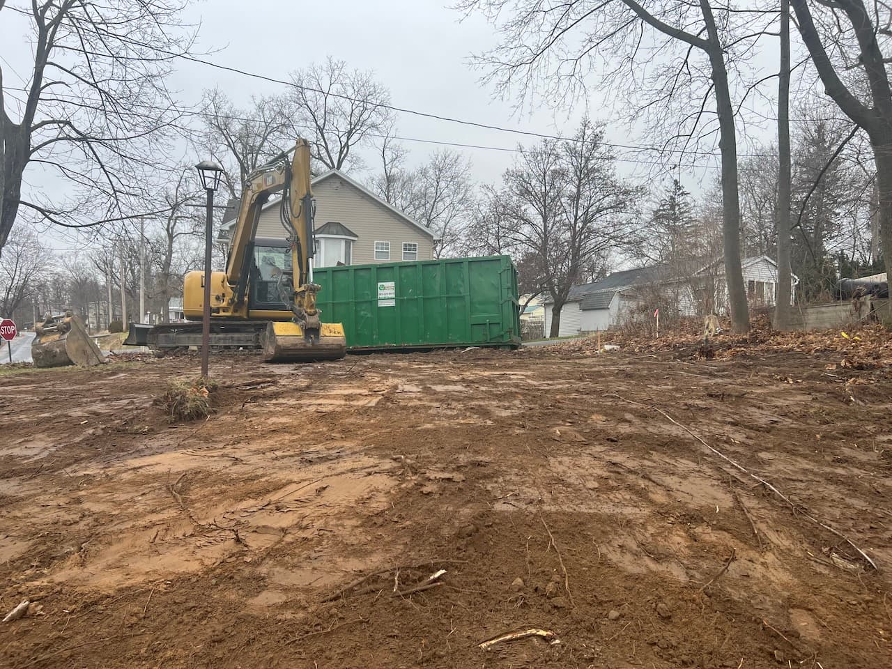 Yellow excavator and green dumpster on cleared construction site