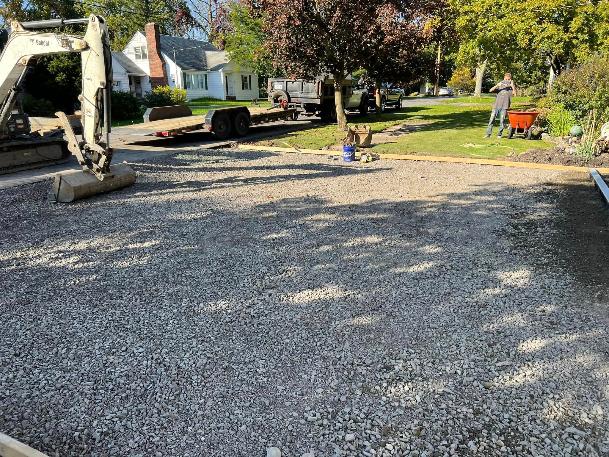 Freshly laid gravel base for driveway with excavator and workers