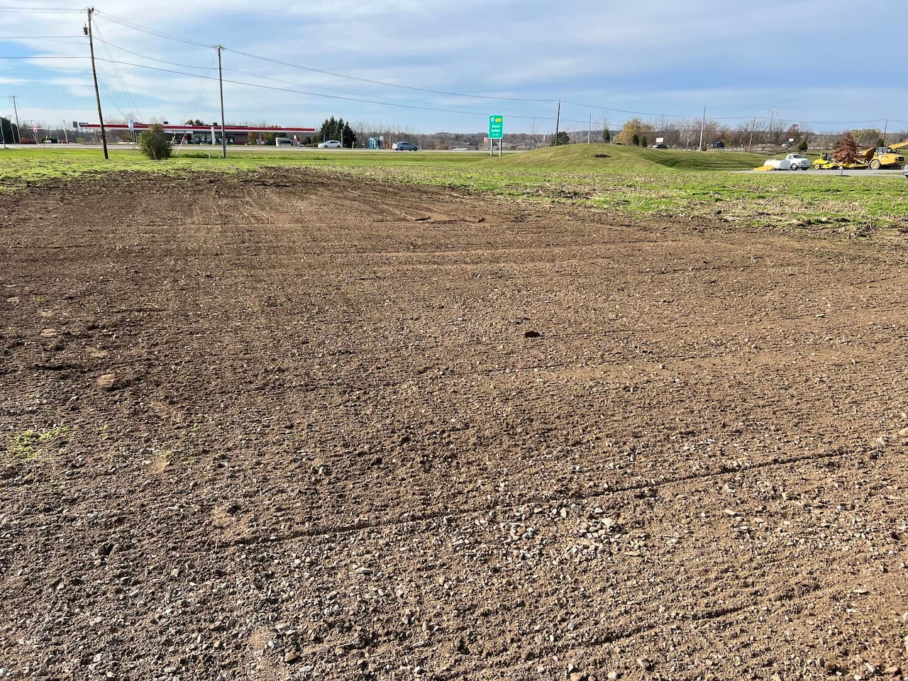 Cleared and graded dirt field prepared for septic system installation with gas station in background
