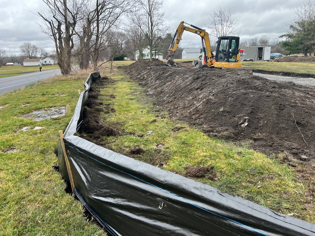 Black silt fence barrier along excavation site with yellow excavator working in background