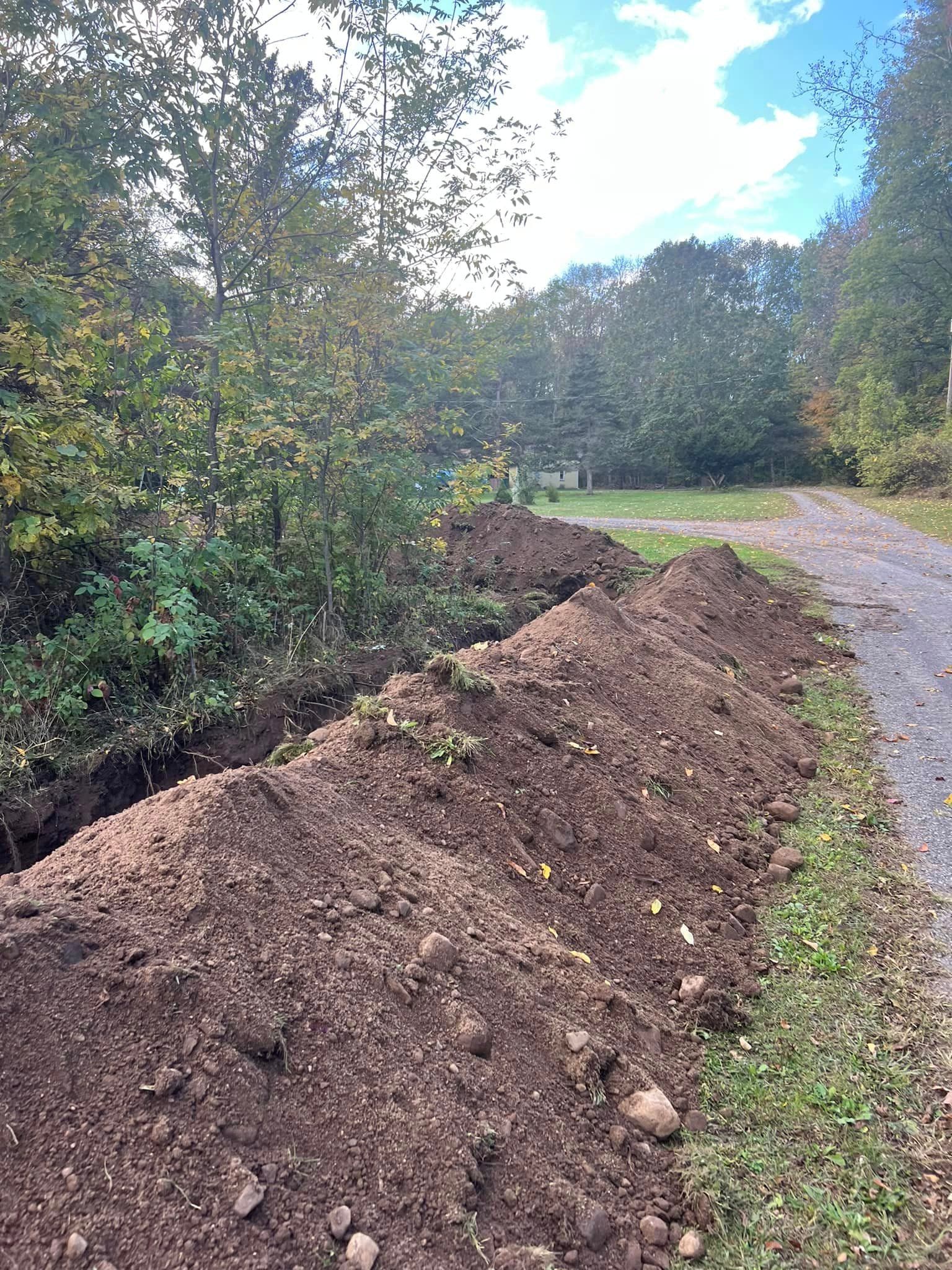Freshly excavated trench with mounds of dirt along paved driveway