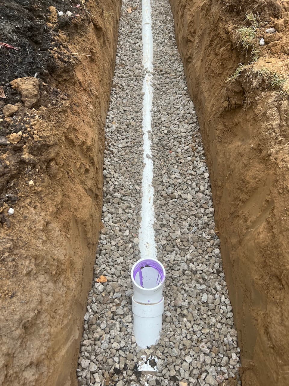 White PVC drainage pipe installed in gravel-filled trench
